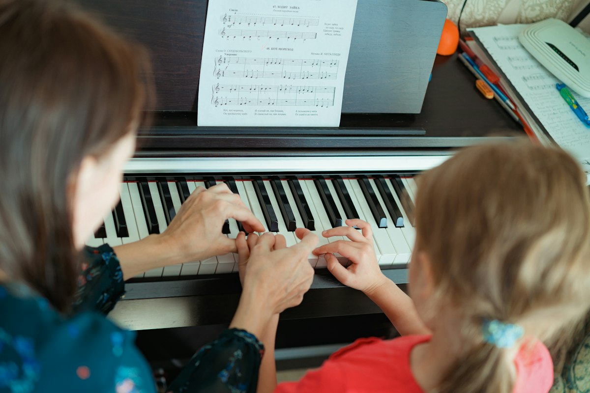 Professora orientando as mãos de uma aluna ao piano durante aula individual